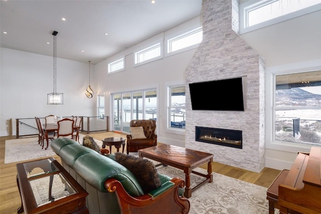 living room with light wood-type flooring, plenty of natural light, a high ceiling, and a stone fireplace