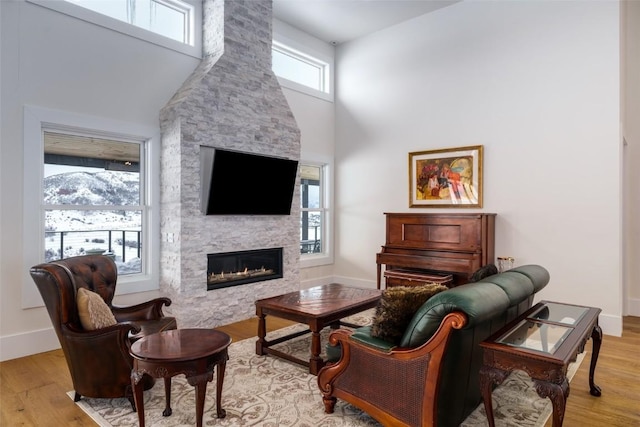 living area with baseboards, a fireplace, a towering ceiling, and light wood-style floors