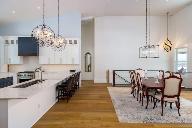 dining space with high vaulted ceiling, an inviting chandelier, light hardwood / wood-style flooring, and sink