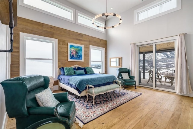 bedroom featuring wooden walls, light hardwood / wood-style flooring, a high ceiling, and access to outside