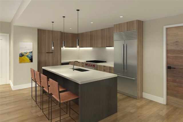 kitchen with sink, built in refrigerator, decorative light fixtures, a kitchen island with sink, and a breakfast bar