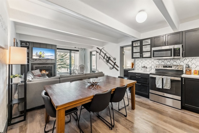 kitchen featuring backsplash, stainless steel appliances, light hardwood / wood-style floors, and beamed ceiling