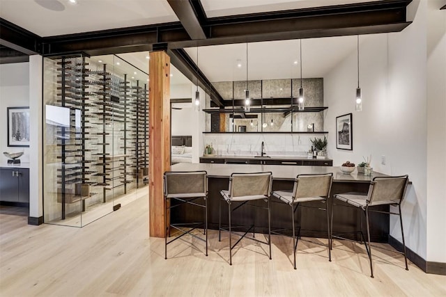 bar featuring decorative backsplash, light hardwood / wood-style flooring, hanging light fixtures, and sink