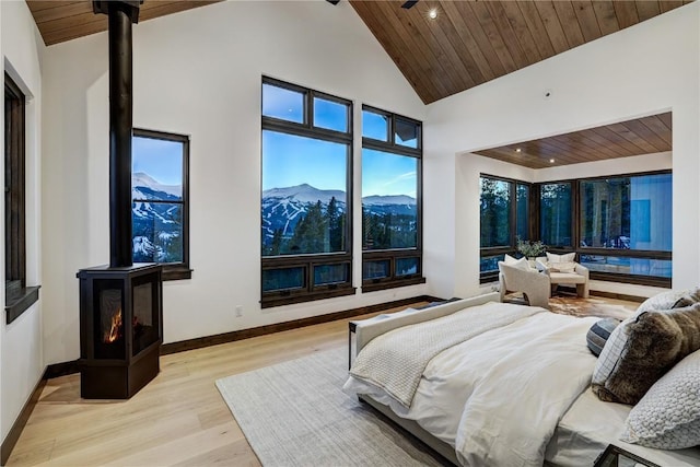 bedroom featuring a mountain view, light wood-type flooring, a wood stove, and wooden ceiling