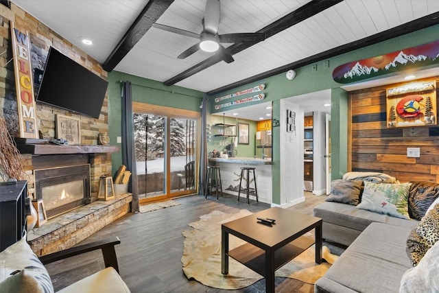 living room featuring beam ceiling, ceiling fan, a fireplace, and wood-type flooring