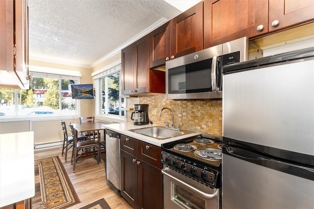 kitchen with appliances with stainless steel finishes, tasteful backsplash, a textured ceiling, sink, and light hardwood / wood-style flooring