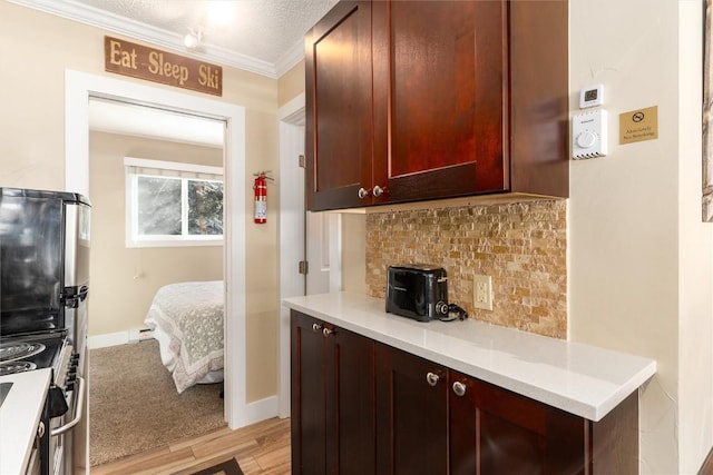 kitchen featuring stainless steel gas range, light hardwood / wood-style flooring, crown molding, fridge, and decorative backsplash