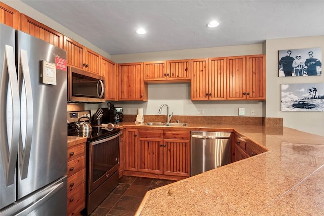 kitchen featuring tile counters, brown cabinetry, appliances with stainless steel finishes, a sink, and recessed lighting