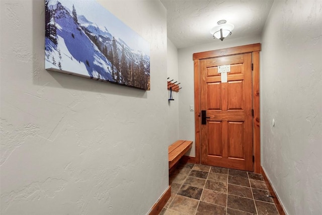 doorway to outside with a textured wall and baseboards