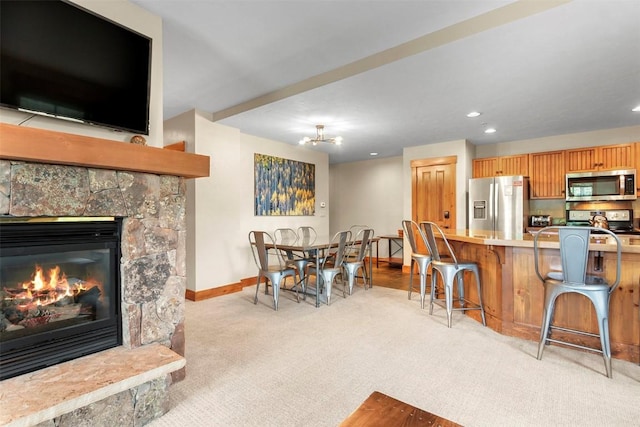 kitchen featuring a breakfast bar area, light colored carpet, stainless steel appliances, a fireplace, and baseboards