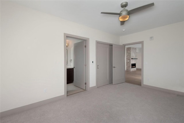 unfurnished bedroom with ceiling fan, a fireplace, connected bathroom, light colored carpet, and a closet