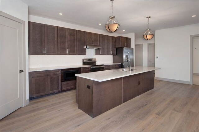 kitchen with appliances with stainless steel finishes, light wood-type flooring, sink, a center island with sink, and hanging light fixtures