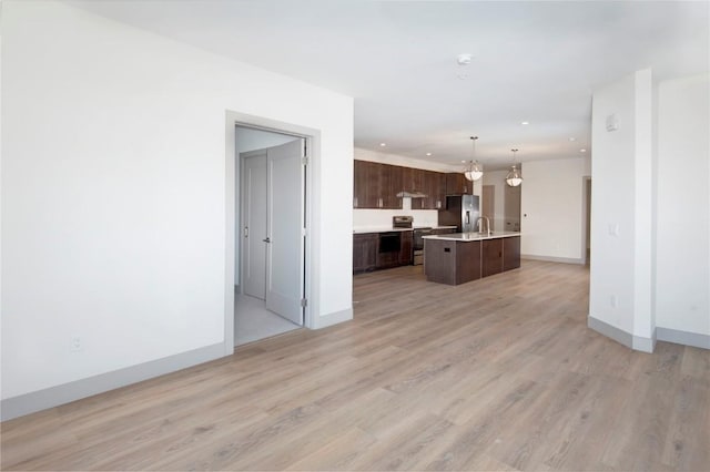 kitchen featuring pendant lighting, light hardwood / wood-style flooring, an island with sink, dark brown cabinetry, and stainless steel appliances