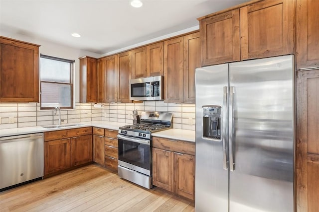 kitchen with decorative backsplash, sink, light hardwood / wood-style floors, and appliances with stainless steel finishes