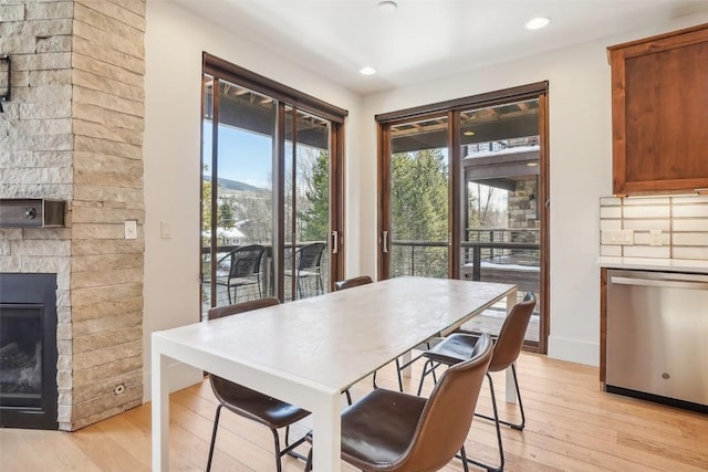 dining room with light wood-type flooring and a stone fireplace