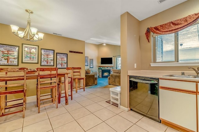 kitchen with decorative light fixtures, a sink, a chandelier, a warm lit fireplace, and dishwasher