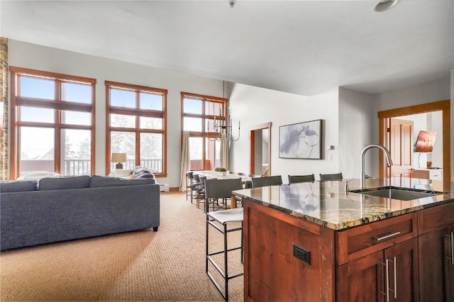 kitchen with a breakfast bar, light colored carpet, open floor plan, a sink, and dark stone countertops