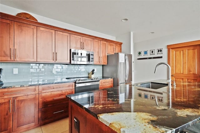 kitchen featuring light tile patterned floors, stainless steel appliances, a sink, backsplash, and dark stone counters