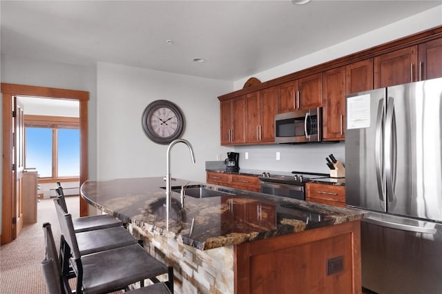 kitchen featuring dark stone countertops, carpet, a kitchen island with sink, stainless steel appliances, and a sink