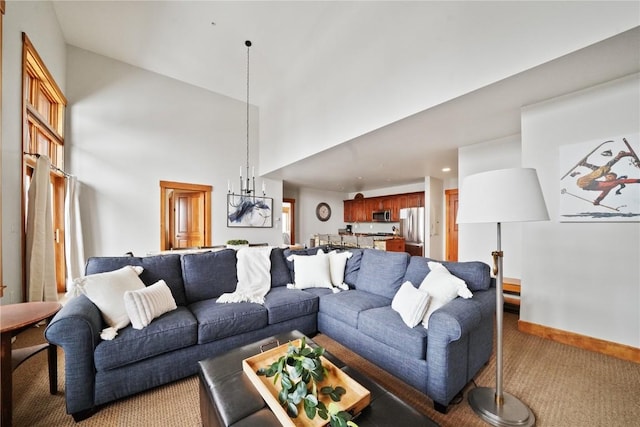 living area with light carpet, a notable chandelier, a towering ceiling, and baseboards