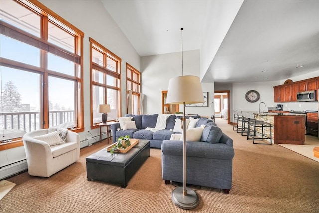 living area with a baseboard radiator, light carpet, plenty of natural light, and a towering ceiling