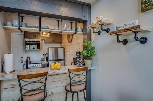 kitchen featuring a breakfast bar, open shelves, a sink, appliances with stainless steel finishes, and a peninsula