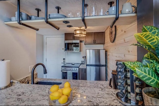 kitchen with light stone counters, wood walls, stainless steel appliances, and a sink