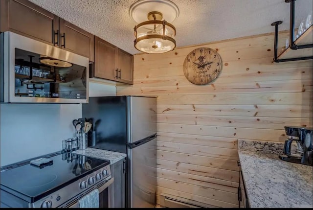 kitchen featuring light stone counters, a textured ceiling, appliances with stainless steel finishes, and wood walls