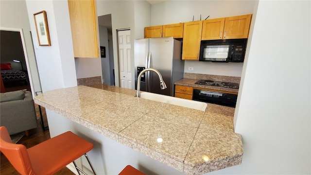 kitchen with tile counters, a peninsula, black appliances, and a kitchen bar