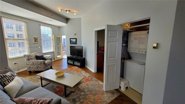 living room featuring baseboards, track lighting, wood finished floors, and stacked washer / drying machine