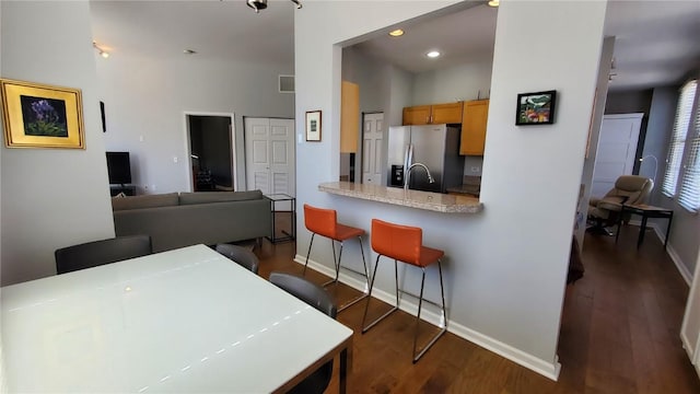 kitchen featuring recessed lighting, dark wood finished floors, baseboards, stainless steel fridge, and a kitchen bar