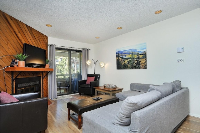 living room featuring wooden walls, a fireplace, wood-type flooring, and a textured ceiling