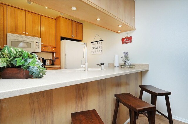 kitchen featuring kitchen peninsula, a breakfast bar, light hardwood / wood-style floors, and white appliances