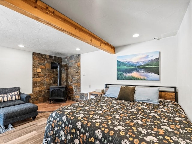 bedroom featuring beamed ceiling, a wood stove, and hardwood / wood-style flooring