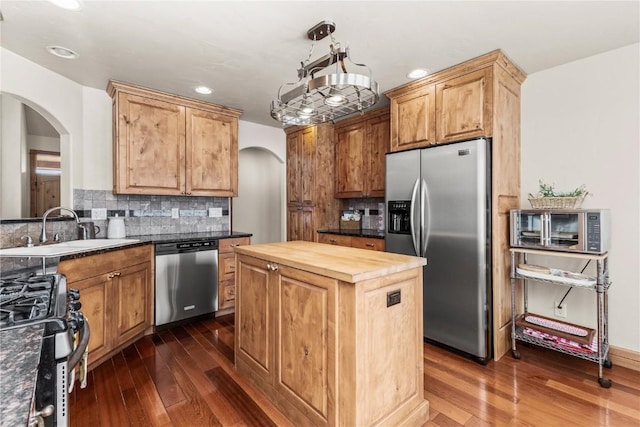 kitchen with arched walkways, butcher block counters, a sink, appliances with stainless steel finishes, and decorative backsplash