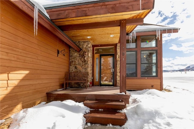 snow covered property entrance with a porch and stone siding