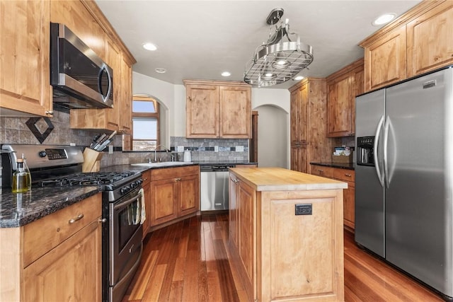 kitchen featuring arched walkways, stainless steel appliances, a sink, wooden counters, and a center island