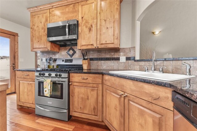 kitchen featuring stainless steel appliances, dark countertops, a sink, and light wood-style flooring