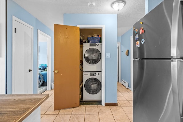 laundry room featuring stacked washer and dryer, light tile patterned flooring, a baseboard heating unit, and a textured ceiling