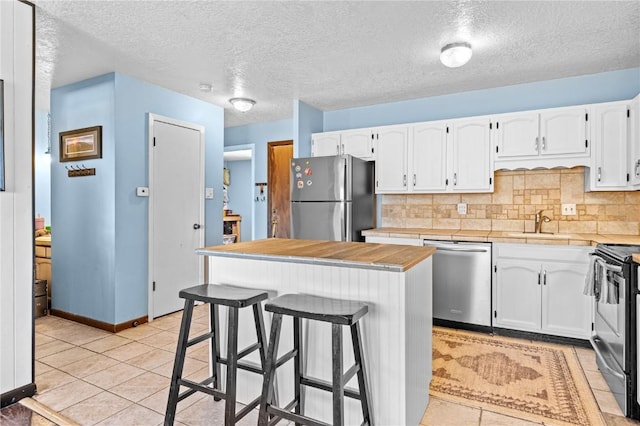 kitchen with stainless steel appliances, light tile patterned flooring, a kitchen island, and white cabinets