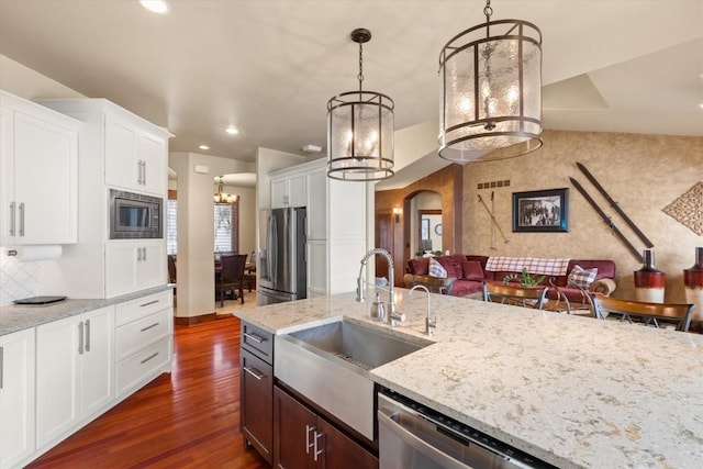 kitchen with arched walkways, dark wood-style flooring, appliances with stainless steel finishes, a sink, and light stone countertops