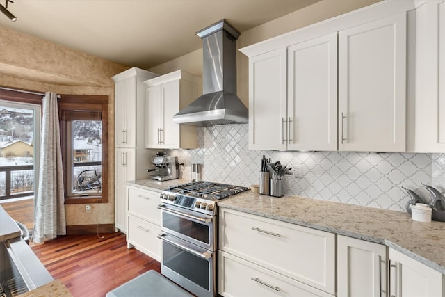 kitchen featuring wood finished floors, white cabinetry, double oven range, wall chimney range hood, and decorative backsplash