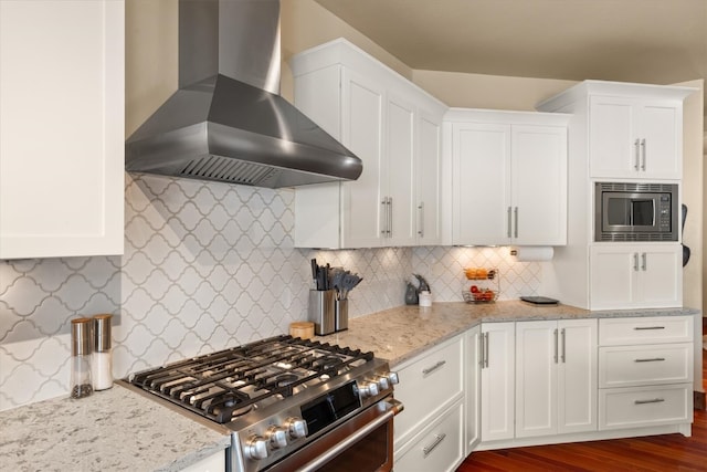 kitchen with light stone counters, dark wood-style flooring, appliances with stainless steel finishes, white cabinets, and wall chimney range hood