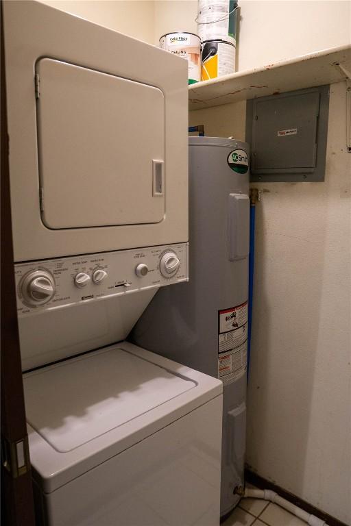 laundry room featuring stacked washer / dryer, water heater, electric panel, and light tile patterned flooring