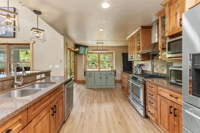 kitchen featuring a sink, appliances with stainless steel finishes, wall chimney range hood, light wood-type flooring, and backsplash