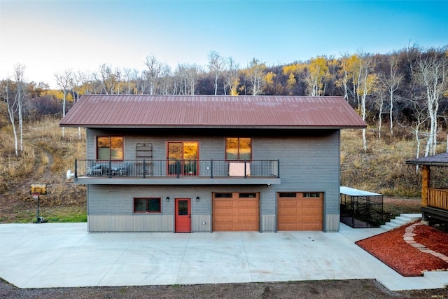 back of house featuring a garage, concrete driveway, a balcony, and metal roof