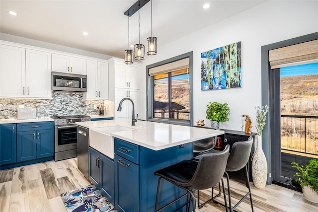 kitchen with a sink, light countertops, appliances with stainless steel finishes, blue cabinets, and tasteful backsplash