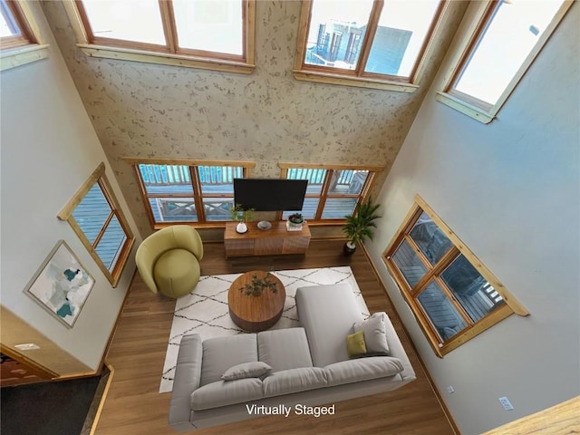 living room featuring wallpapered walls, a high ceiling, and wood finished floors