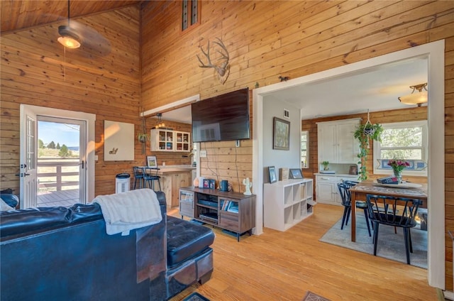 living area featuring light wood-style flooring, high vaulted ceiling, and wood walls