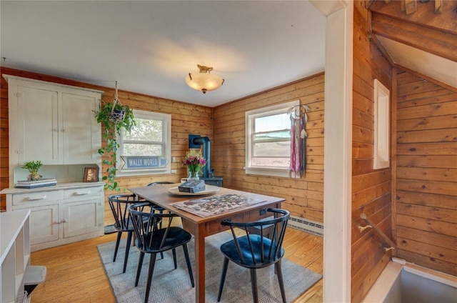 dining space featuring light wood-style flooring, wood walls, and a baseboard radiator